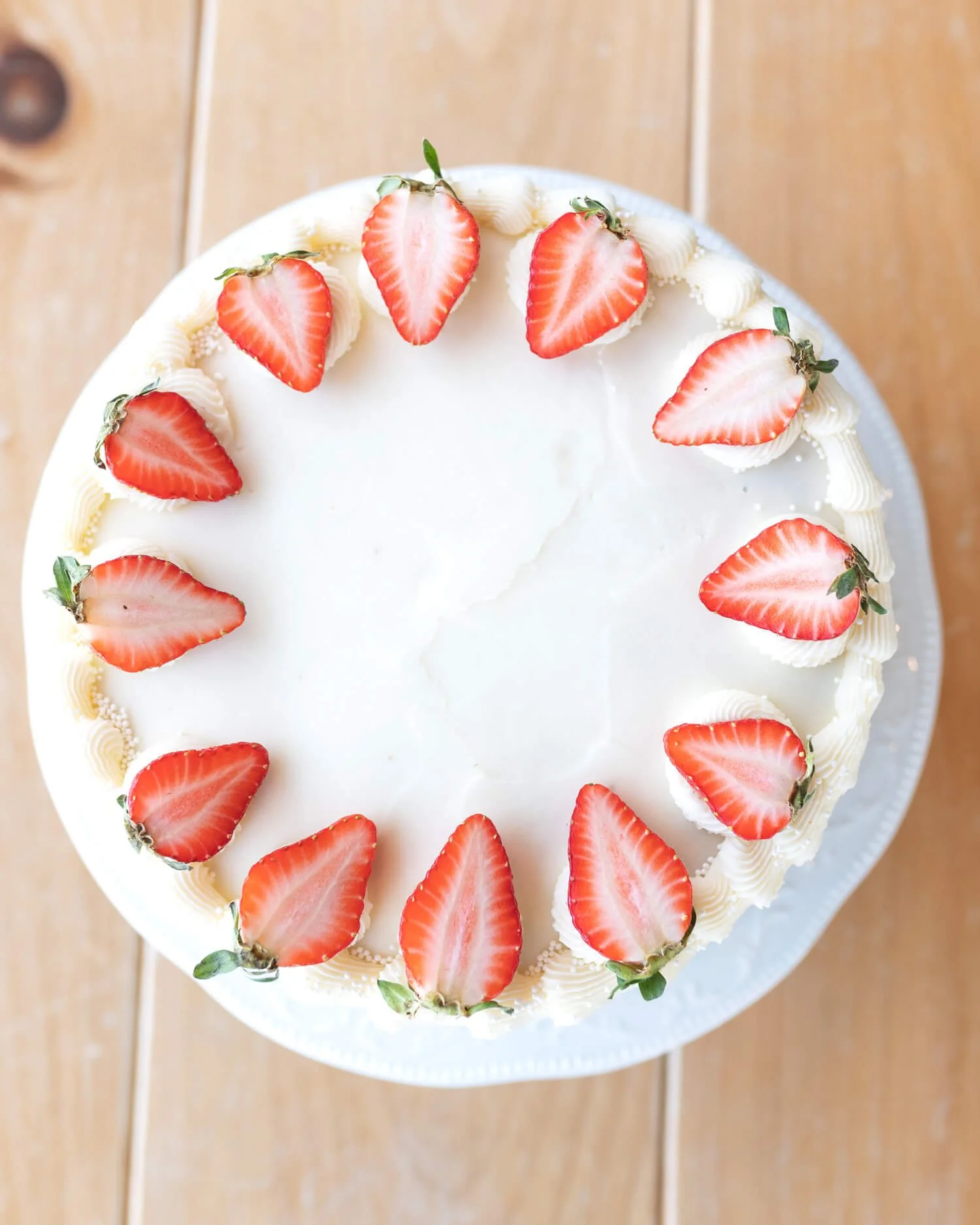 A white buttercream cake ringed with fresh strawberries, seen from above