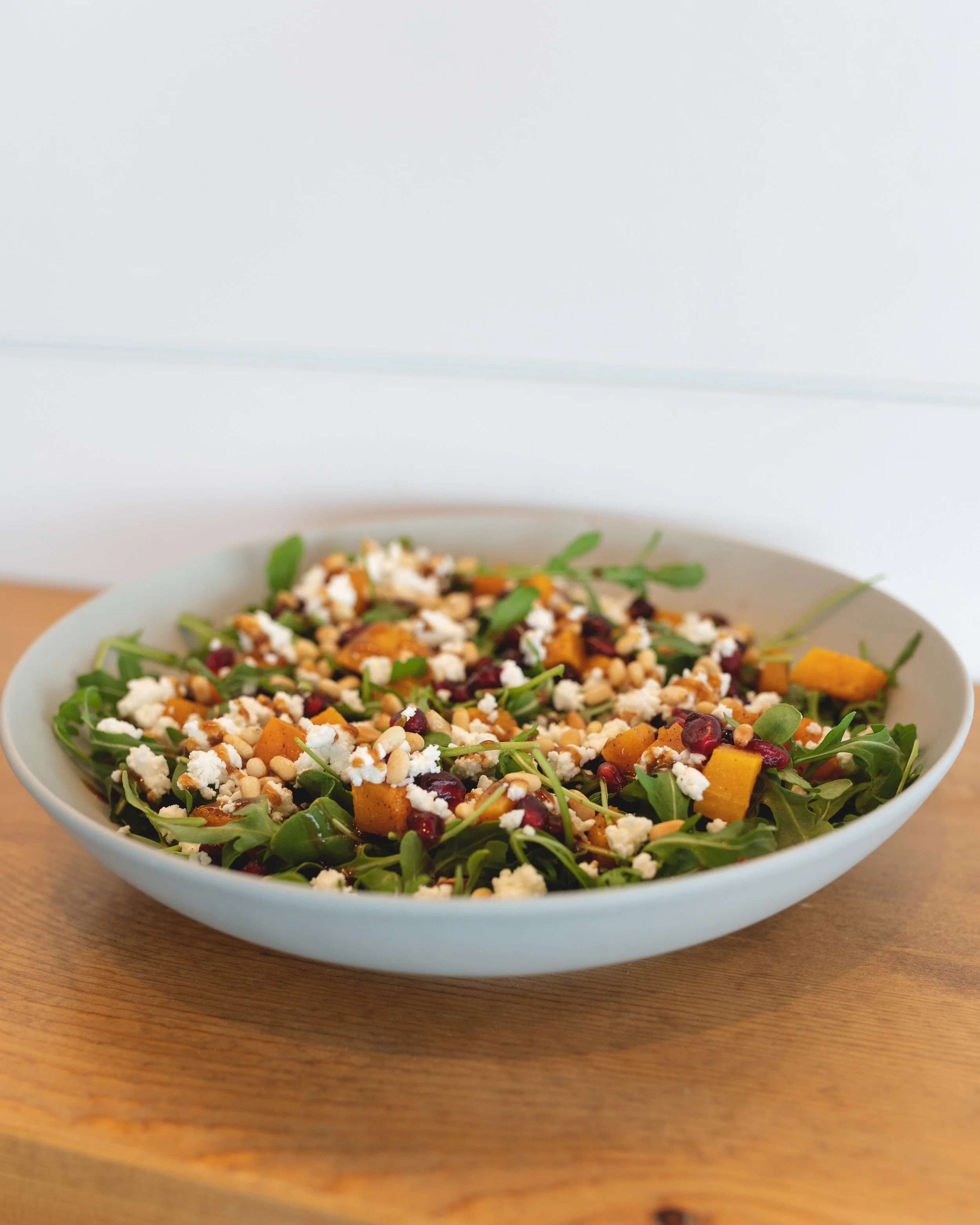 A bowl of arugula salad with roasted squash, feta, pine nuts and cranberries
