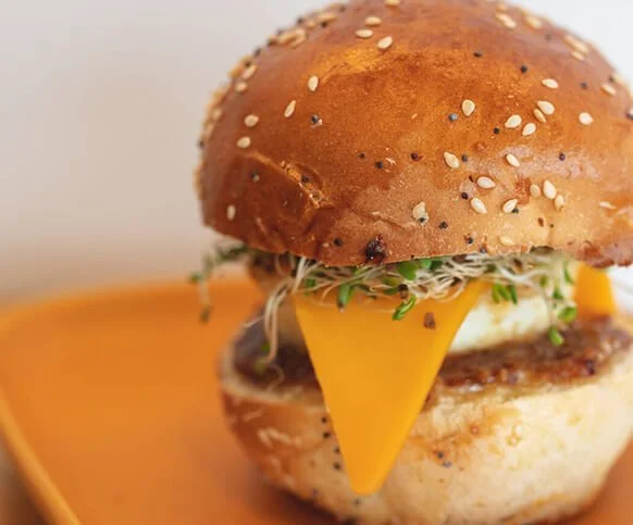 A breakfast sandwich with cheddar, egg and sprouts on a seeded brioche bun